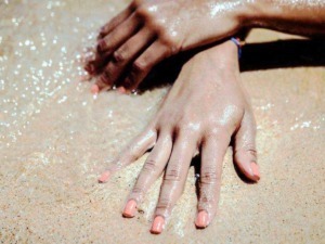 Mani mani con unghie curate e smalto rosa su spiaggia di sabbia dorata sotto la luce del sole, scena di relax e divertimento estivo.