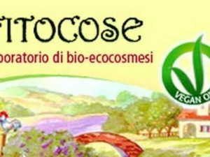 Bio-ecosmesi laboratorio naturale di fitocose con simbolo vegano, eco sostenibilità e prodotti vegani senza crueltà, ambientato in un paesaggio rurale con natura e architettura tradizionale.