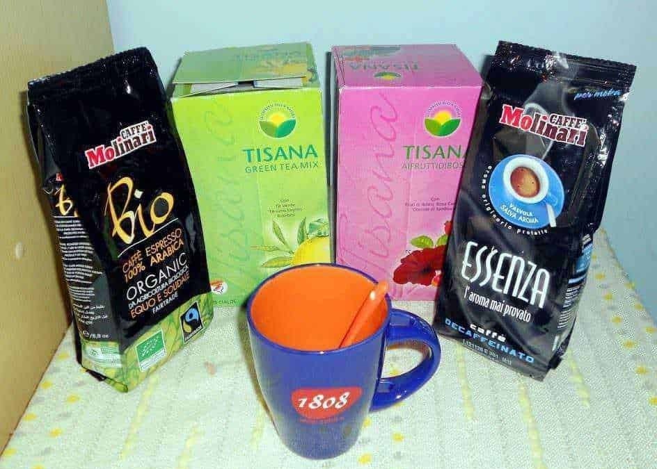 Tè verde e tisane in scatola con caffè biologico in confezioni colorate, tazza da tè blu con cucchiaino arancione.
