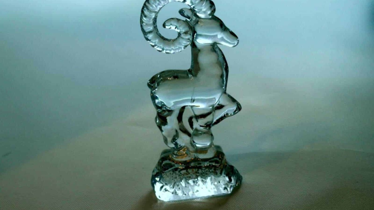 Riflesso di una scultura in vetro a forma di capra con corna arcuate e dettagli trasparenti, simbolo artistico in vetro decorativo.