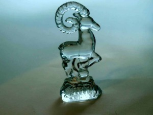 Riflesso di una scultura in vetro a forma di capra con corna arcuate e dettagli trasparenti, simbolo artistico in vetro decorativo.