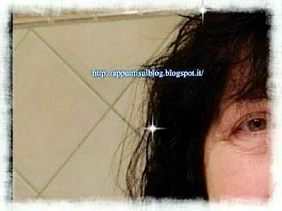 Lunghi capelli neri e volto sorridente, primo piano di una donna con sfondo di piastrelle beige. Immagine brillante e coinvolgente per blog o articoli di lifestyle e bellezza.
