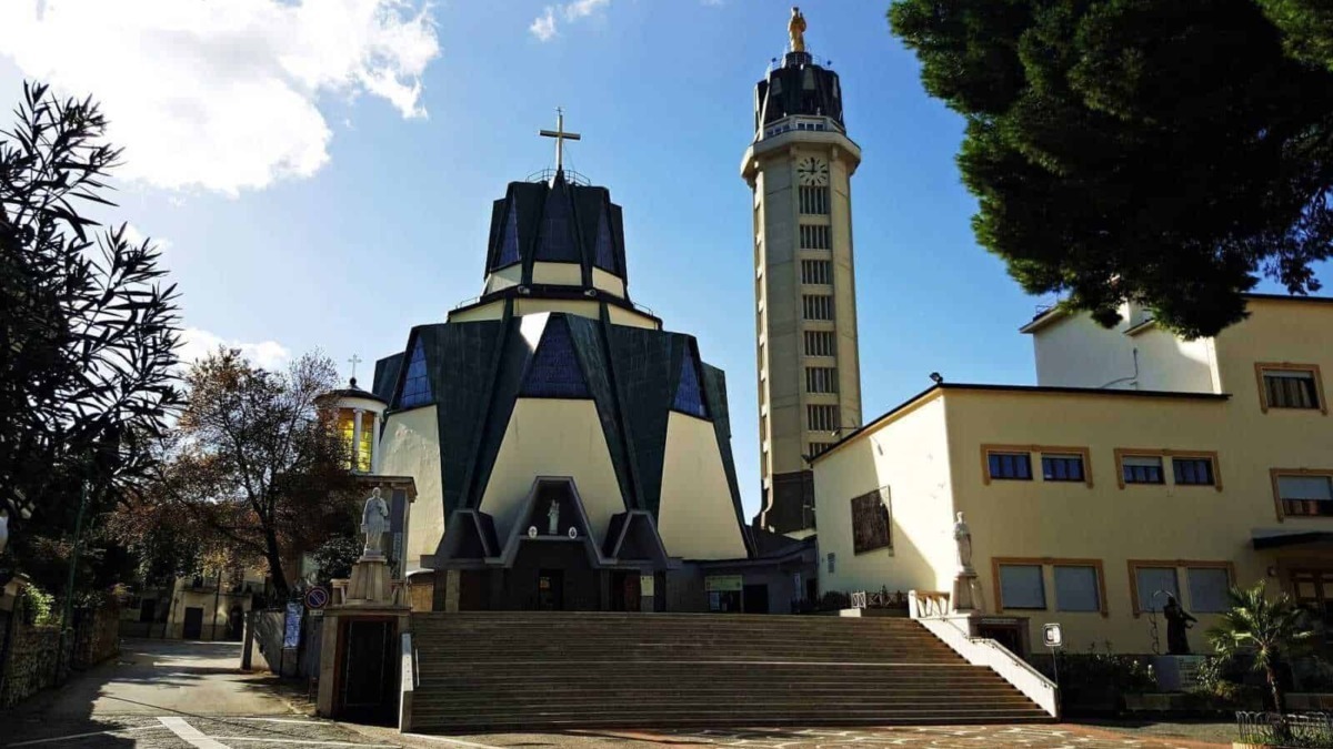 Chiesa moderna con architettura audace e torre campanaria, situata in un contesto urbano con alberi e scalinate, rappresenta un esempio di architettura religiosa innovativa in Italia.