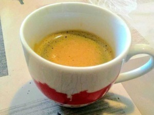Tazza di caffè espresso cremoso in tazza decorata con disegni rossi, su una tovaglietta con motivi naturali, perfetta per appassionati di caffè e lifestyle quotidiano.