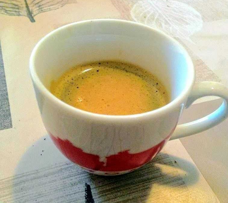 Tazza di caffè espresso cremoso in tazza decorata con disegni rossi, su una tovaglietta con motivi naturali, perfetta per appassionati di caffè e lifestyle quotidiano.