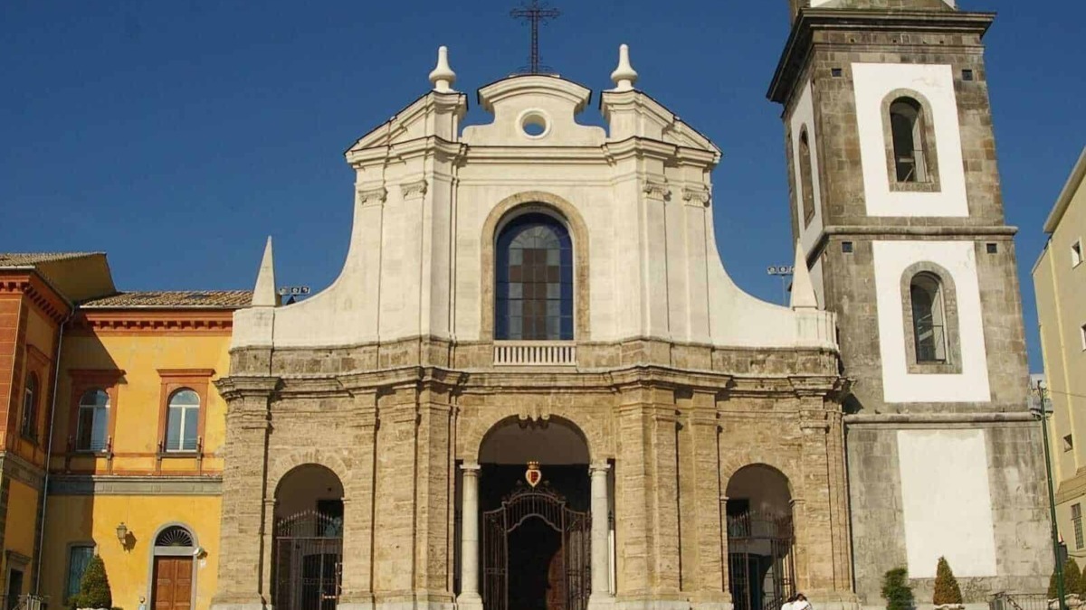 Elegante chiesa barocca con facciata in pietra e torre campanaria, situata in un contesto urbano con edifici colorati e un cielo sereno.