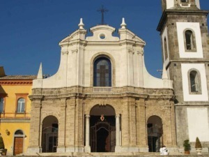 Elegante chiesa barocca con facciata in pietra e torre campanaria, situata in un contesto urbano con edifici colorati e un cielo sereno.