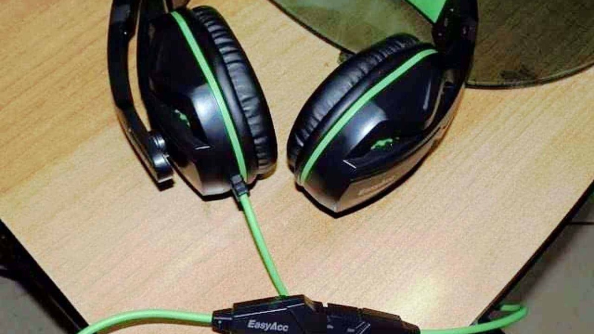 Auricolari gaming con microfono e cavo verde, headset over-ear nere e verdi per gaming e streaming, collocati su un tavolo di legno nero, accessori elettronici gaming.