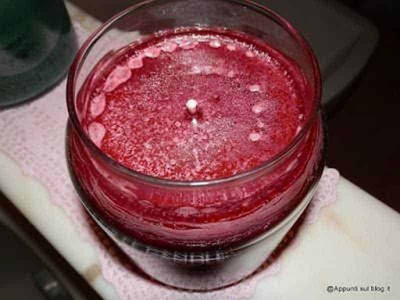Fragranza di candela viola con cera solida in vasetto di vetro, ambientata in un contesto domestico elegante e accogliente.