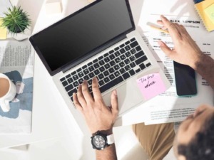 Le immagini di un workspace con laptop, appunti e smartphone, rappresentano un ambiente di lavoro digitale, ideale per freelance e professionisti, focalizzato su produttività.