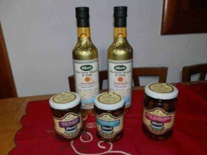 Olio extra vergine di oliva e conserve di olive Alberti, prodotti tipici italiani, su tovaglia rossa in cucina.