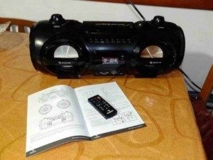 Riproduttore stereo portatile nero con manuale e telecomando su tavolo in legno.