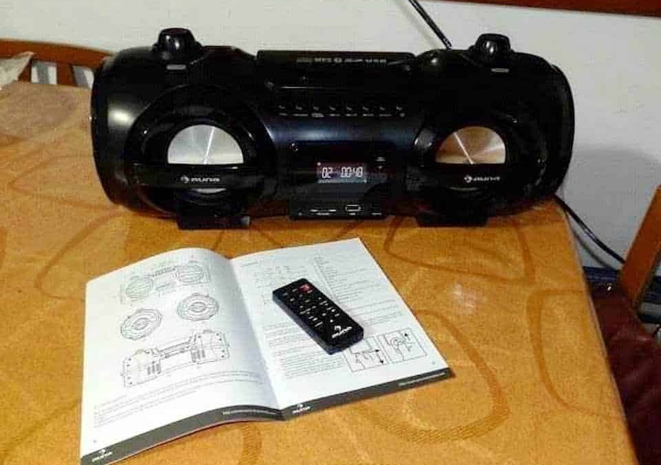 Riproduttore stereo portatile nero con manuale e telecomando su tavolo in legno.