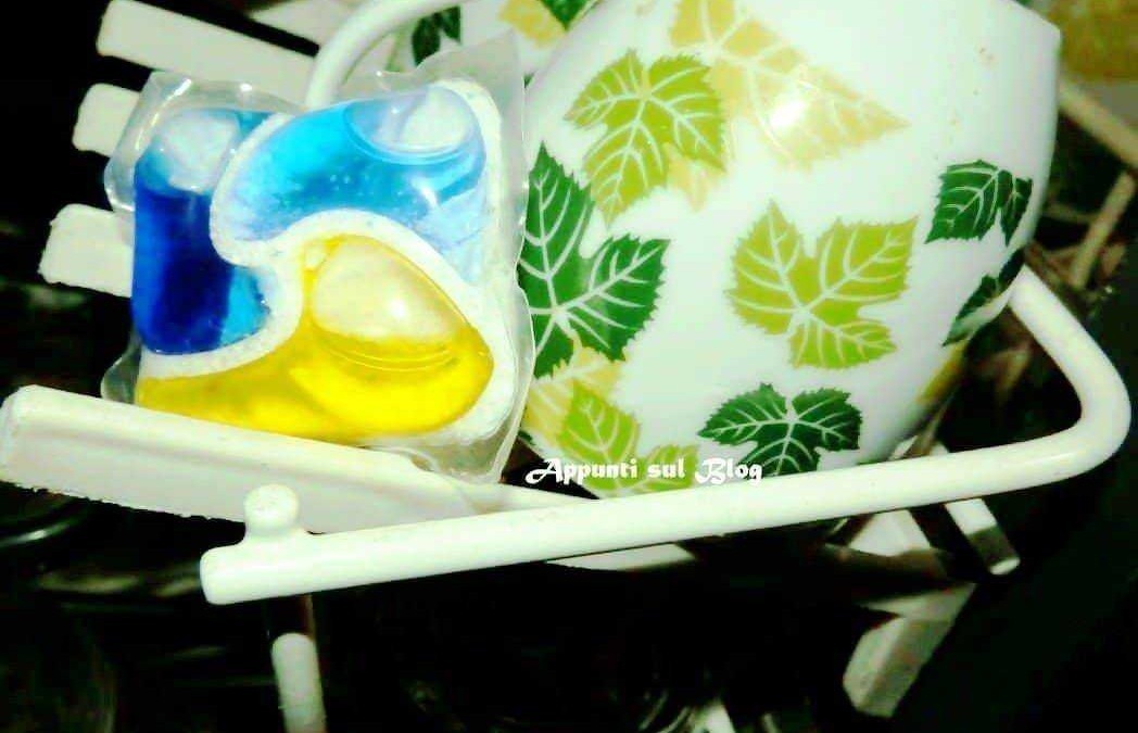 Vaschetta con piatti e tazze in ceramica decorata con foglie verdi e gialle, con saponi colorati, posizionata su un supporto bianco, ideale per l'uso quotidiano in cucina o in casa.