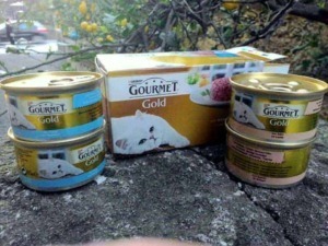 Gourmet Gold cibo per gatti scatole e lattine di cibo umido per felini, immagine con confezioni di alimenti feline di alta qualità.