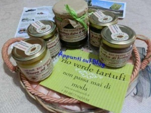 Bocconi di tartufo verde in piccoli barattoli di vetro su un cesto di vimini, con un cartello informativo che invita a conoscere il prodotto raro e di tendenza.