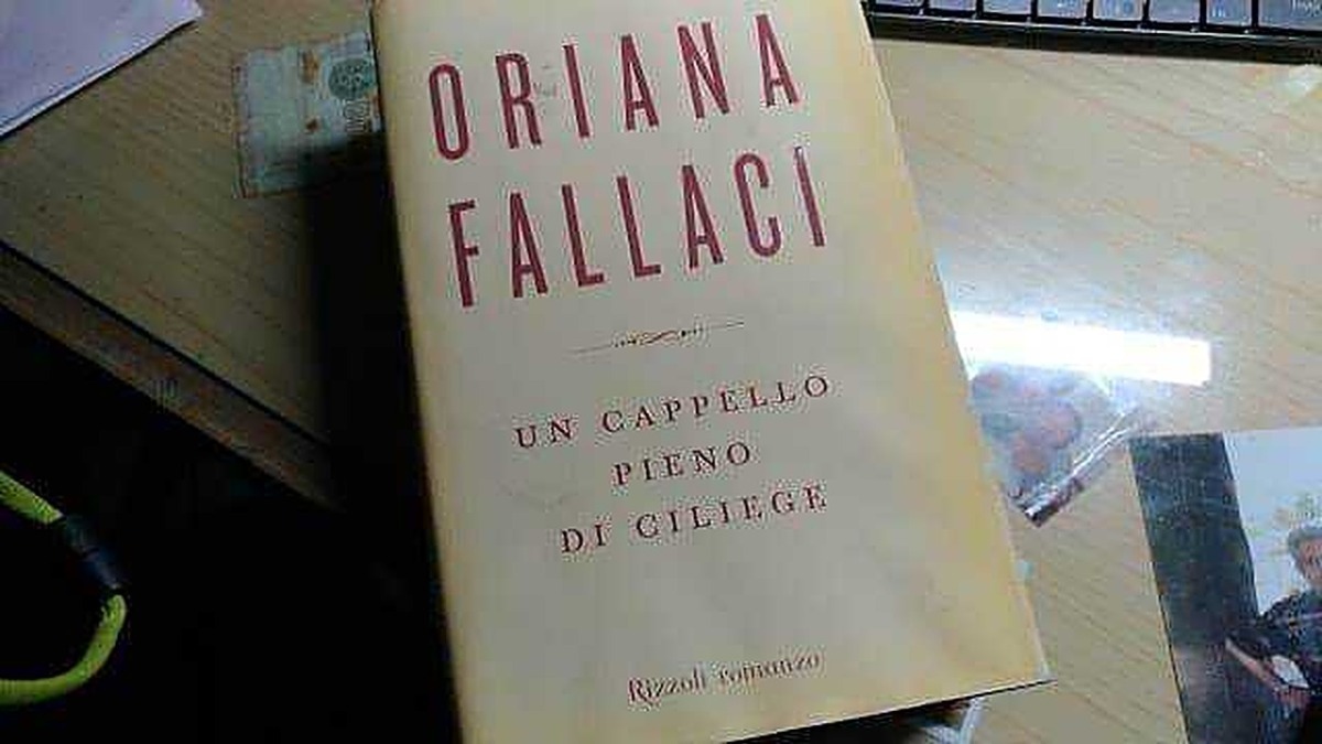 Copertina del libro "Un cappello pieno di college" di Oriana Fallaci, foto di un libro su un tavolo con altri materiali di scrittura.