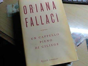 Copertina del libro "Un cappello pieno di college" di Oriana Fallaci, foto di un libro su un tavolo con altri materiali di scrittura.