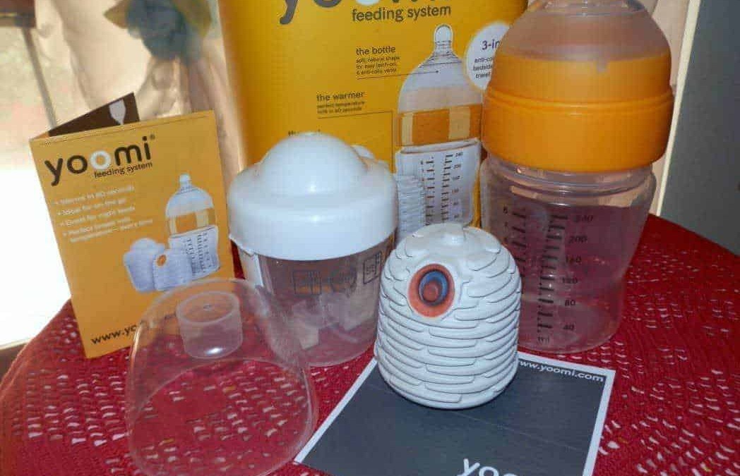 Pompa alimentazione biberon Yoomi, sistema di riscaldamento automatico per latte, accessori per allattamento, pratici e innovativi prodotti per neonati, sul tavolo con caraffa e scatola.