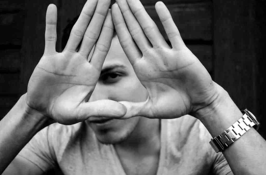 - Hands form a triangle around one eye, black and white photo.