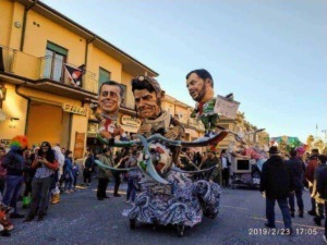 Carro allegorico con testine giganti durante una parata mascherata in strada in occasione di un carnevale, pubblico che osserva e partecipa alla festa, atmosfera vivace e colorata.