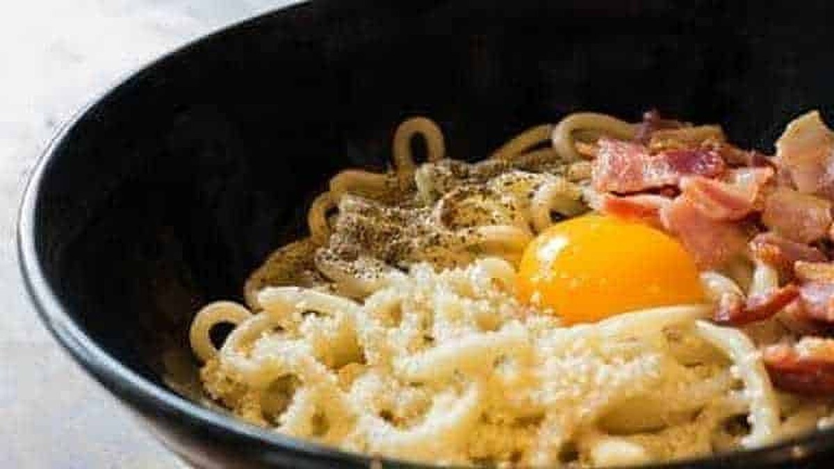Uova, pancetta e formaggio sulla pasta in una ciotola nera, primo piatto tradizionale italiano.