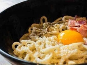 Uova, pancetta e formaggio sulla pasta in una ciotola nera, primo piatto tradizionale italiano.
