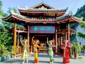 Architettura tradizionale asiatica con corso di danza folkloristica all'aperto vicino a montagne verdi e vegetazione rigogliosa.