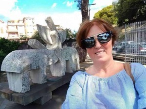 Scultura moderna in pietra con donna con occhiali da sole sorridente in primo piano alla fermata dell'autobus all'aperto in città.