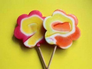 Lollipop a forma di fiore multicolore su sfondo giallo brillante.