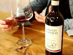 Profumo di vino rosso in una degustazione italiana, bottiglia di Chianti Classico Monostoli e calice sul tavolo in un ambiente informale. Perfetto per chi apprezza i vini toscani autentici.