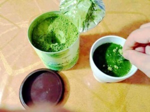 Polvere di erbe verdi in barattoli e una tazza con piante di erba fresca, simbolo di prodotti naturali e benessere.