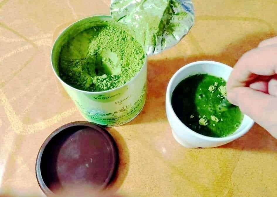Polvere di erbe verdi in barattoli e una tazza con piante di erba fresca, simbolo di prodotti naturali e benessere.