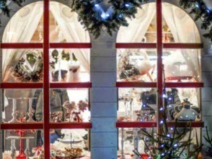 Addobbi natalizi e decorazioni di Natale viste da una finestra di una casetta di legno con tende, luci e ornamenti festivi, creando un'atmosfera calda e accogliente per le festività.