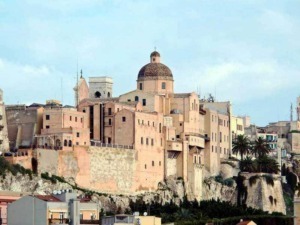 Palazzo storico e edificio religioso su una collina a Valetta, Malta, con veduta panoramica, cielo nuvoloso e palme.