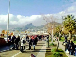 Passeggiata sul lungomare di Napoli con vista sul Vesuvio, persone che si godono una giornata di sole, ambiente vivace e accogliente nel centro città.