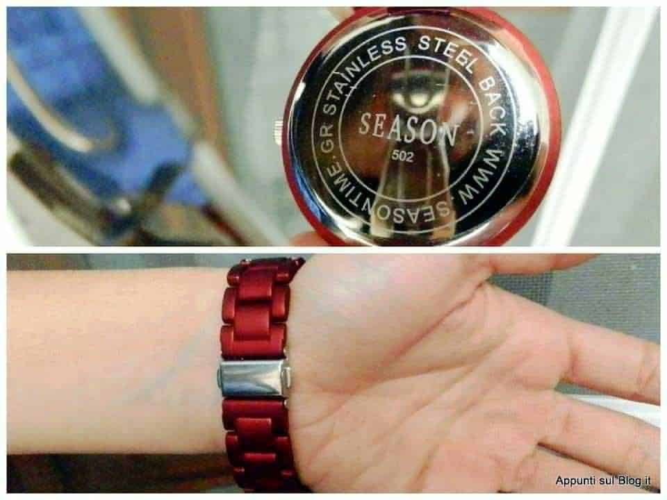 Orologio da donna rosso con cinturino in metallo e cinturino, con pietre colorate e quadrante bianco, indossato su un polso di donna con sfondo di fontana e giardino.