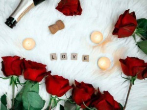 Roses rosse, candele accese, e lettere a formare la parola "LOVE" su un morbido sfondo bianco, creando un'atmosfera romantica e suggestiva per occasioni speciali o momenti di affetto.