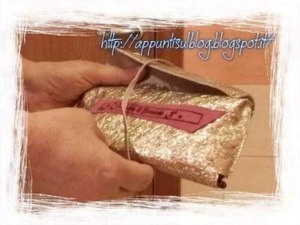 Foglietto regalo di Natale avvolto in carta dorata con un fiocco dorato, ideale per regali di lusso e occasione speciale.