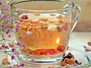 Tè alle erbe infuso con fiori essiccati, in una tazza di vetro trasparente circondata da fiori di campo viola e petali secchi, ideale per rilassarsi e favorire il benessere.