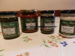 Barattoli di conserve di frutta e verdura fatte in casa, con etichette che indicano sambuco, gelatina di fichi, cassis e rosa canina, su tovagliolo floreale.
