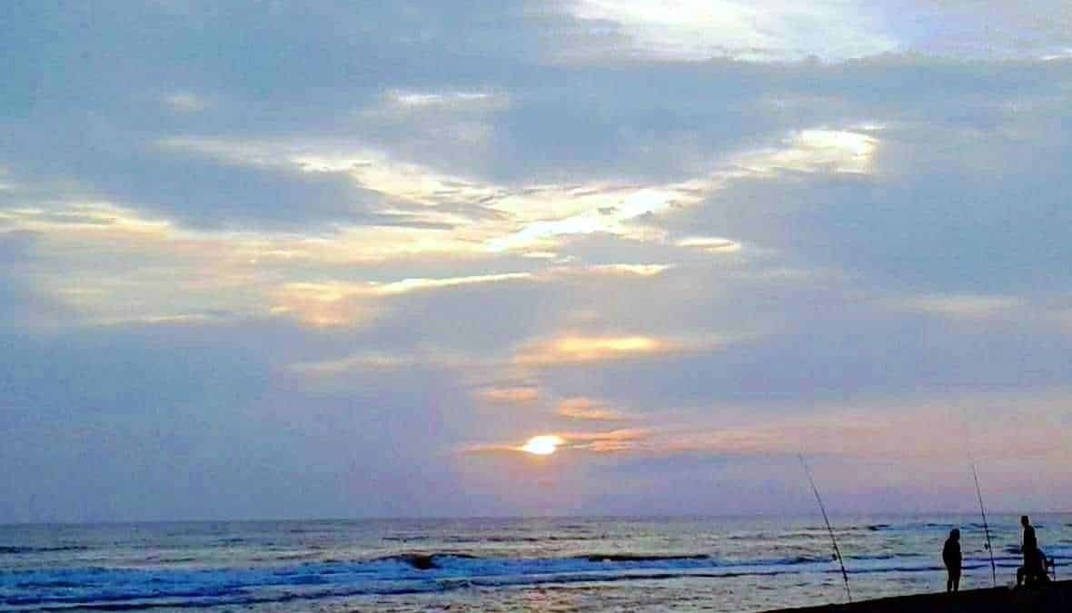 Tramonto sulla spiaggia con due persone che pescano, cielo blu e nuvole, atmosfera rilassante, perfetta per momenti di relax e pesca sul mare, fotografia di paesaggio marino.