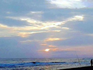 Tramonto sulla spiaggia con due persone che pescano, cielo blu e nuvole, atmosfera rilassante, perfetta per momenti di relax e pesca sul mare, fotografia di paesaggio marino.