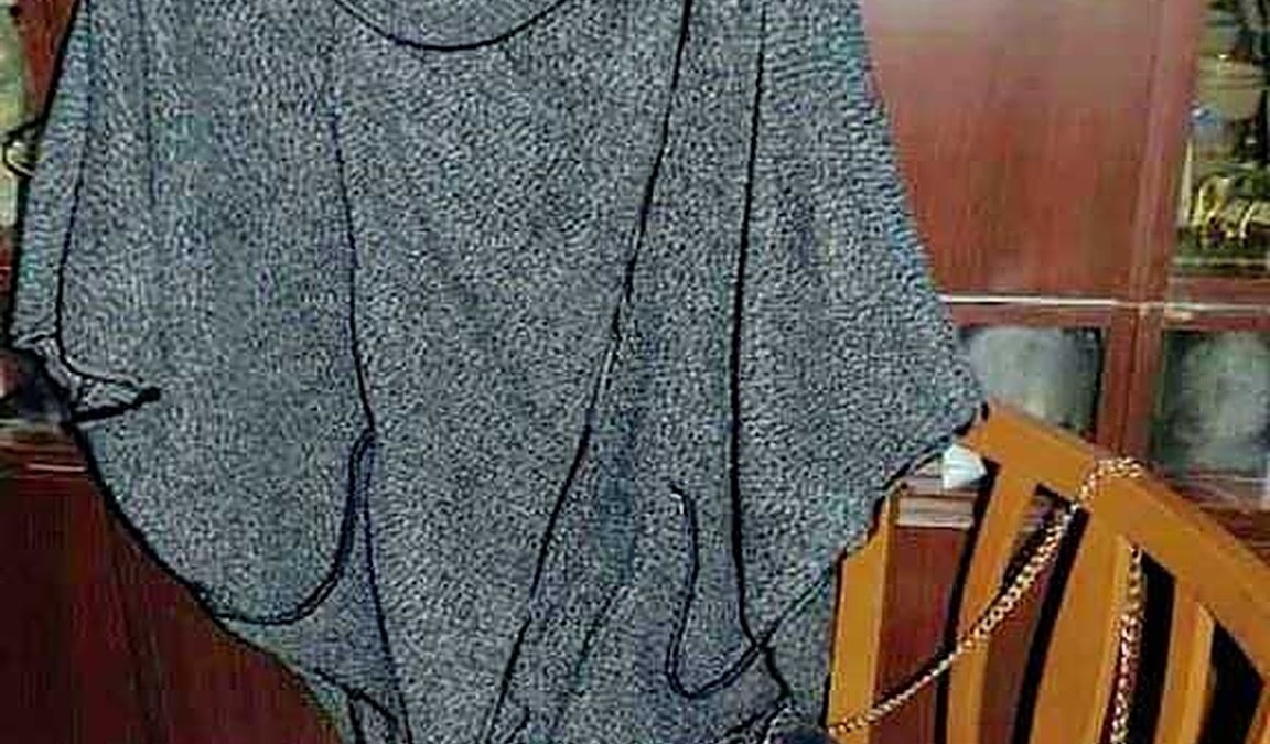 Oversized grey knit poncho with black piping, hanging on a wooden hanger.