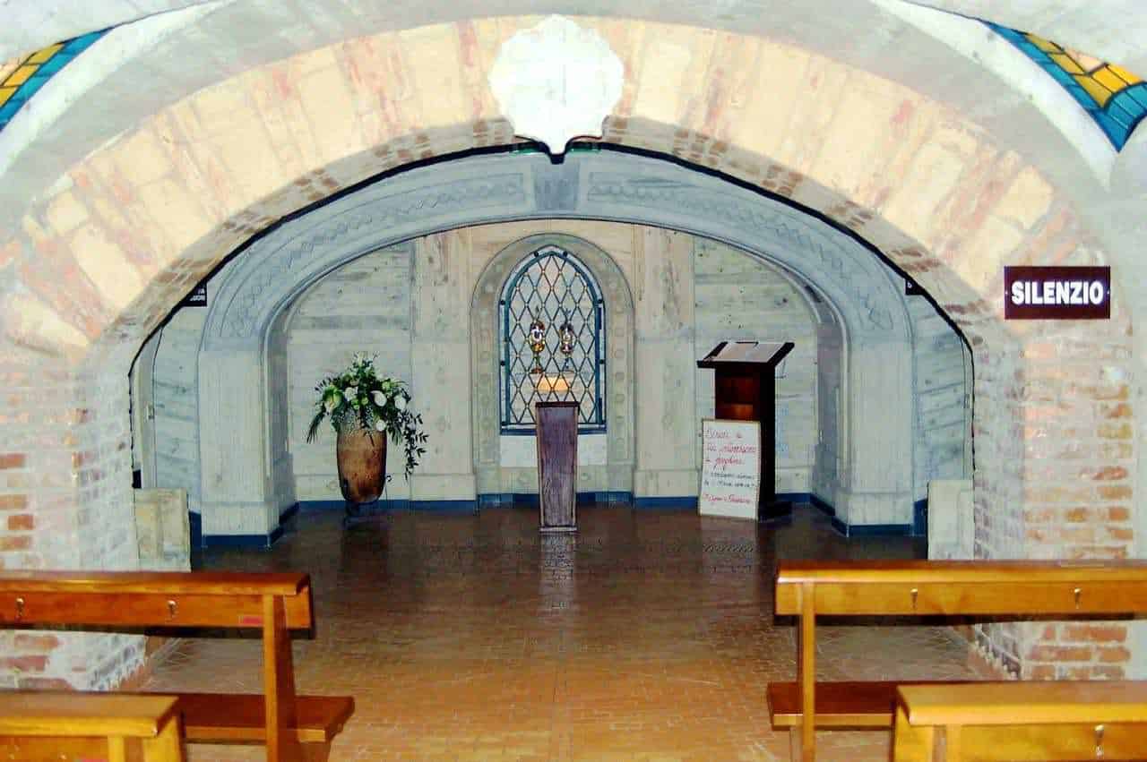 Silenzio, cappella storica con arredi in legno, vaso di fiori e finestra con vetrata decorativa, ambiente sacro tranquillo, ideale per meditazione e preghiera, foto di un luogo di spiritualità.
