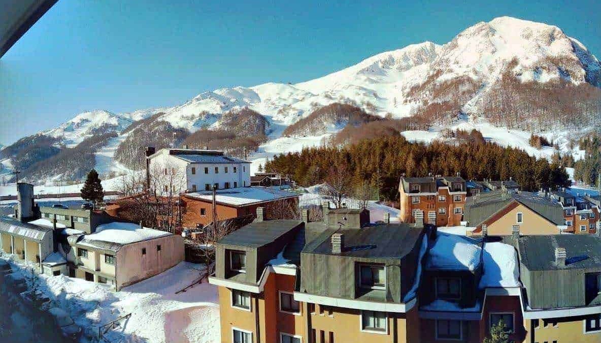Valle innevato con case e montagna sullo sfondo, scena di montagna invernale con edifici e natura, foto di un paesaggio alpino innevato in Italia, perfetto per blog su viaggi e natura.