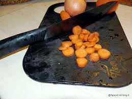 Carote affettate su tagliere in cucina, preparazione di ingredienti freschi per ricetta, coltello nero, comodo e affilato.