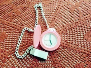 Orologio da cucina rosa con catena, posato su una superficie di feltro arancione rugoso, simbolo di puntualità e tempo per il blog Appunti Sul Blog.