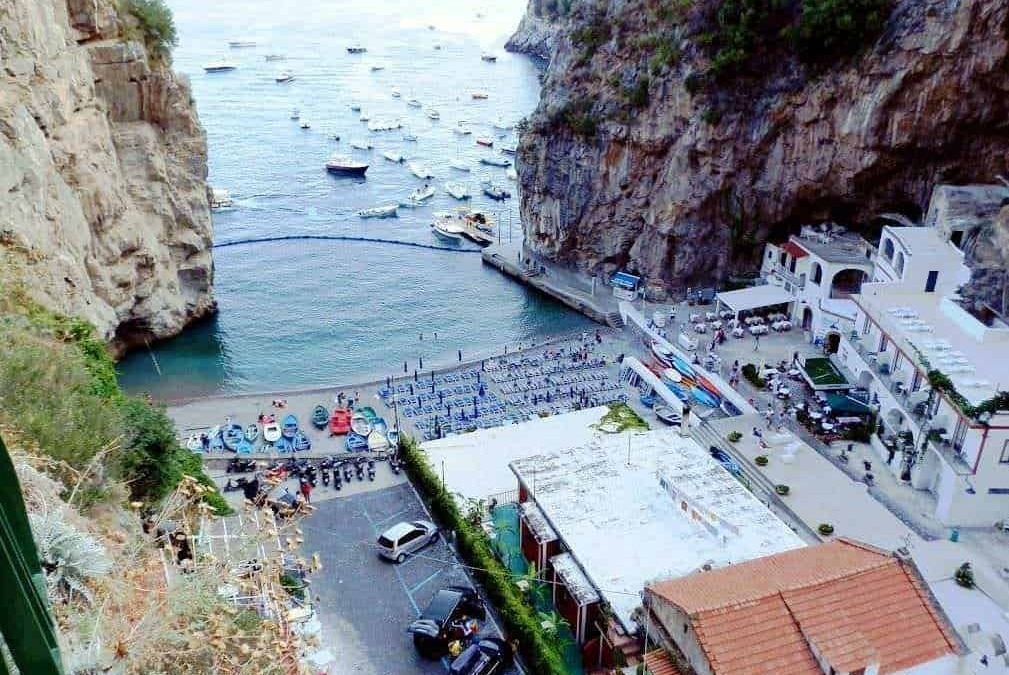 Spiaggia con barche e scogliere a Positano, Costa Amalfitana, vista dall'alto con ristoranti e negozi sul lungomare. Perfetta destinazione turistica per vacanze al mare e relax.