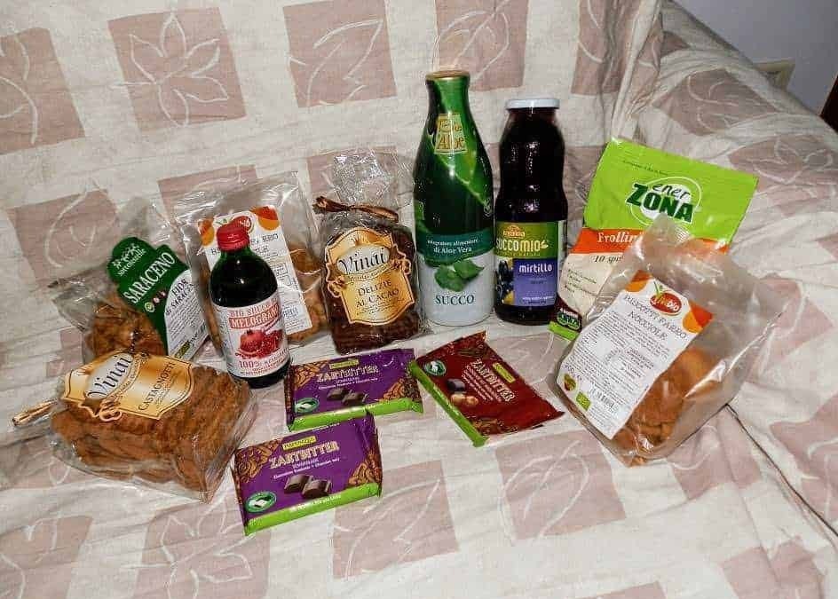 Pane integrale e prodotti da forno biologici, snack salutari, succhi di aloe vera e integratori naturali su un letto con copriletto a fantasia; prodotti alimentari naturali e biologici.